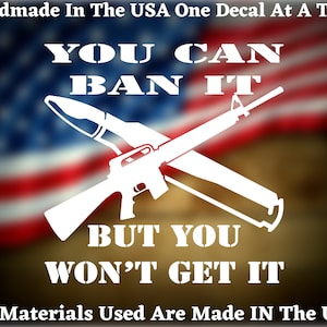 May include: White decal featuring a rifle and a rocket, with the text "YOU CAN BAN IT BUT YOU WON'T GET IT." The background shows a blurred American flag. The text "Handmade In The USA" is at the top, and "All Materials Used Are Made IN The USA" is at the bottom.