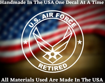 May include: White decal featuring the U.S. Air Force emblem with the text "RETIRED" inside a circle. The words "Handmade In The USA One Decal At A Time" and "All Materials Used Are Made In The USA" are also present. The background is a blurred American flag.