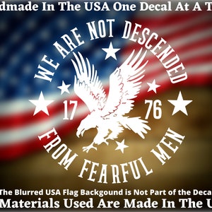 May include: White vinyl decal with a bald eagle, stars, and the text "WE ARE NOT DESCENDED FROM FEARFUL MEN" and "1776". The decal is on a blurred background of the American flag.