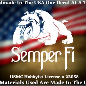 May include: White vinyl decal of a bulldog with the words "Semper Fi" and "USMC Hobbyist License # 22058" below. The decal is on a blurred background of the American flag.