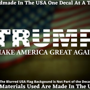 May include: White vinyl decal with the text "TRUMP" in all caps with stars inside the letters and the text "MAKE AMERICA GREAT AGAIN" below. The decal is on a blurred background of an American flag.