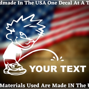 May include: White vinyl decal of a cartoon boy peeing with the text "YOUR TEXT" below. The decal is on a blurred background of an American flag.