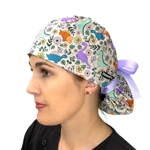 May include: A light purple and white scrub hat with a dinosaur and floral print. The hat has a purple tie.
