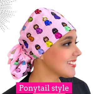 May include: Pink ponytail style scrub cap with a repeating pattern of pregnant woman emojis in various skin tones and hair colors. The cap has a pink ribbon tie. The text "Ponytail style" is in a pink rectangle at the bottom.