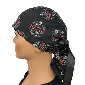 Puede incluir: Gorro quir&uacute;rgico negro con un patr&oacute;n repetido de esqueletos y el texto "Have The Day You Deserve" en un dise&ntilde;o circular. El gorro tiene una cinta negra. El dise&ntilde;o incluye acentos rosas, blancos y turquesas.