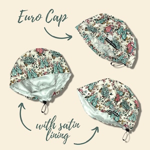 May include: Euro cap with a floral pattern in teal, pink, and cream. The cap has a satin lining and a drawstring closure. The text "Euro Cap" is above the cap, and "with satin lining" is below.