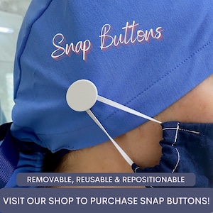 Puede incluir: Primer plano de una gorra quir&uacute;rgica azul con las palabras "Snap Buttons" en una fuente de escritura. Un bot&oacute;n de presi&oacute;n blanco est&aacute; sujeto a la gorra con bandas el&aacute;sticas, conectando a una mascarilla azul. El texto en la parte inferior dice "REMOVABLE, REUSABLE & REPOSITIONABLE".