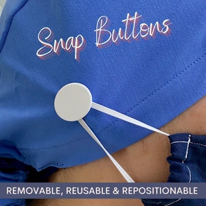 May include: A blue surgical scrub hat with white snap buttons and the text "Snap Buttons" in pink. The hat is worn by a person and the white elastic strap is attached to the buttons. The text below the hat reads "REMOVABLE, REUSABLE & REPOSITIONABLE".
