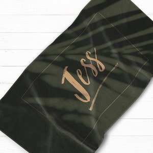 May include: A dark green beach towel with a gold frame and the name "Jess" written in gold script.