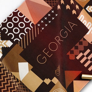 May include: A geometric pattern fabric with the word "GEORGIA" in gold lettering. The fabric features a variety of shapes and colors, including brown, tan, and red.