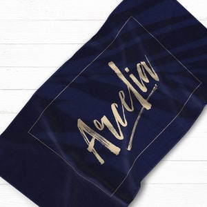May include: A navy blue beach towel with a gold rectangle border and the name "Aurelia" written in gold script.
