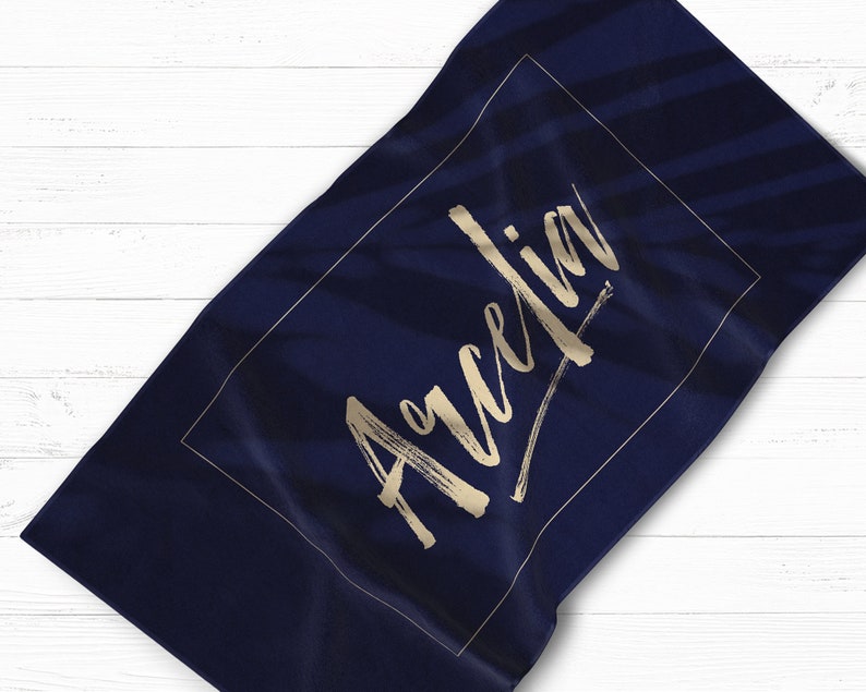May include: A navy blue beach towel with a gold rectangle border and the name "Aurelia" written in gold script.