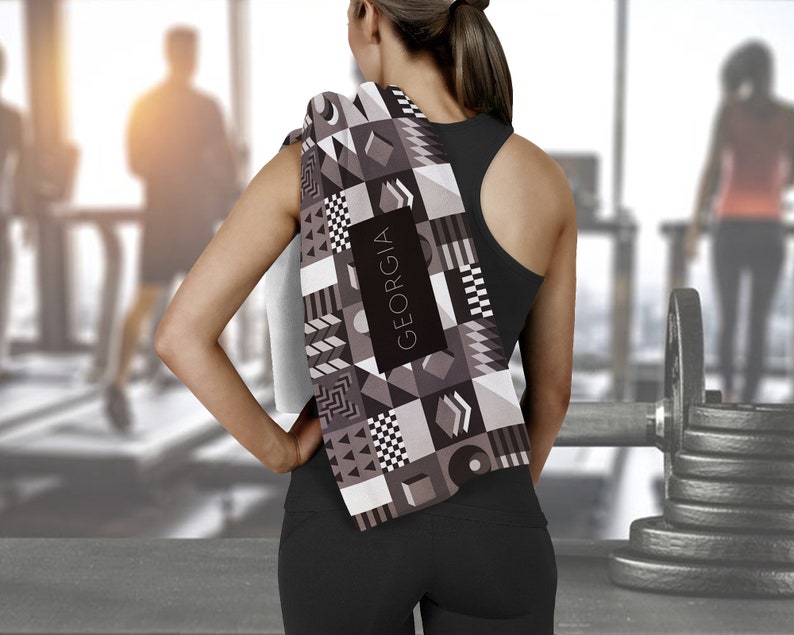 May include: A black and white geometric patterned towel with the word "GEORGIA" printed on it. The towel is draped over the shoulder of a person wearing a black tank top.