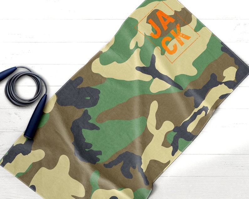 May include: Camouflage-patterned towel with the name "JACK" in orange block letters. A dark blue and gray jump rope is in the image. The towel has a green, brown, and black pattern.