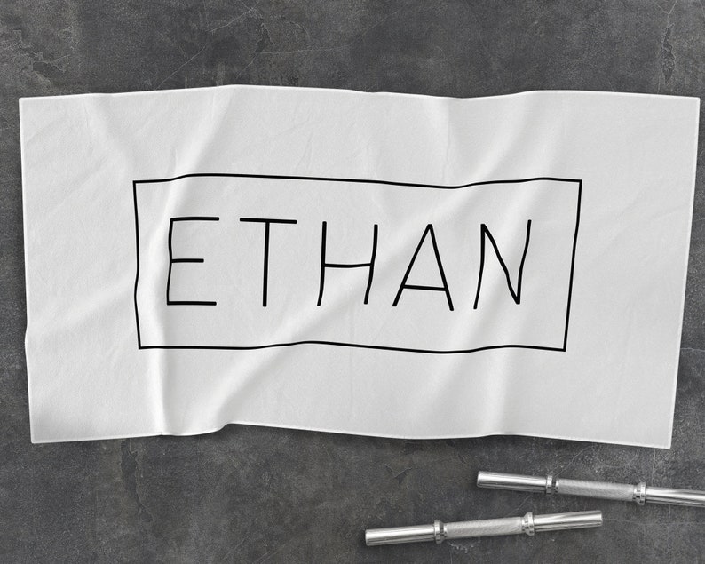 K&ouml;nnte beinhalten: Wei&szlig;es Baumwollhandtuch mit schwarzem Text, der "ETHAN" innerhalb eines schwarzen Rechtecks lautet.