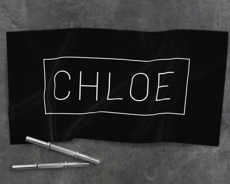K&ouml;nnte beinhalten: Schwarzes Handtuch mit wei&szlig;em Rand und dem Wort "CHLOE" in wei&szlig; innerhalb des Randes.
