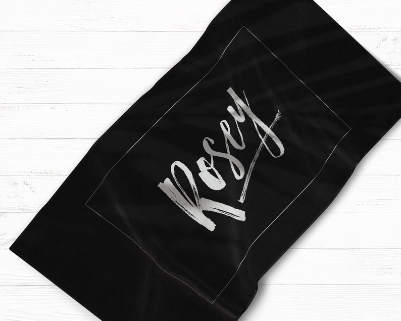 May include: Black beach towel with a white border and the name "Rosey" written in a silver script font.