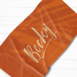 May include: Orange beach towel with the name "Becky" written in a white cursive font.
