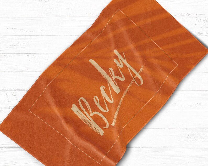 May include: Orange beach towel with the name "Becky" written in a white cursive font.