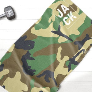 May include: Camouflage-patterned towel with the name "JACK" in a white box. The towel features a green, brown, and black camouflage design. A 25-pound dumbbell is in the background.