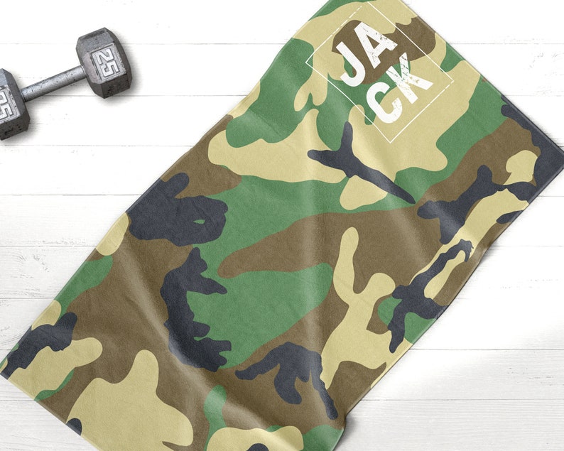 May include: Camouflage-patterned towel with the name "JACK" in a white box. The towel features a green, brown, and black camouflage design. A 25-pound dumbbell is in the background.
