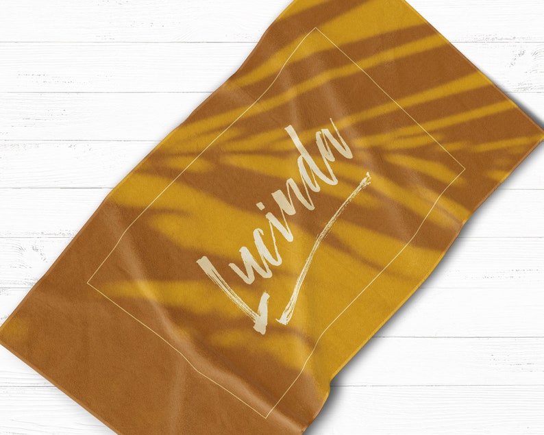 May include: A yellow beach towel with a white palm leaf pattern and the name "Lucinda" written in white cursive script.