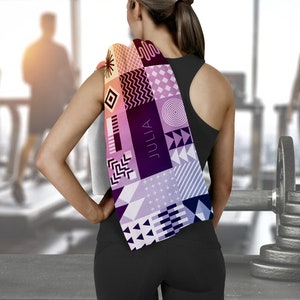 May include: A woman wearing black workout clothes with a colorful patterned towel draped over her shoulder. The towel has geometric shapes and the word "JULIA" printed on it.