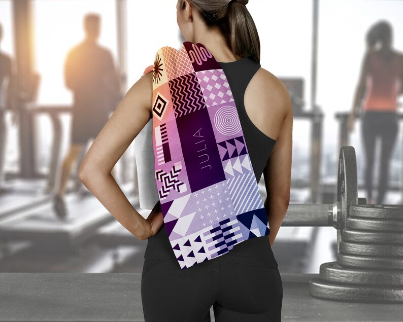 May include: A woman wearing black workout clothes with a colorful patterned towel draped over her shoulder. The towel has geometric shapes and the word "JULIA" printed on it.