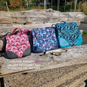 May include: Three crossbody bags in different sizes: S, Original, and XL. The bags feature floral and leaf patterns in shades of pink, blue, and teal. Each bag has a black base and a top handle. The image also includes the text "MELODY CROSSBODY BAG + ADD-ON PDF PATTERN."