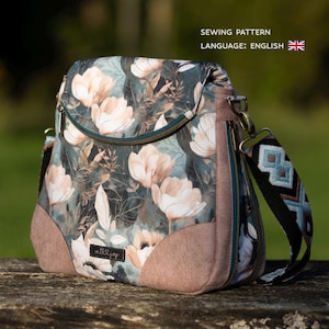 Puede incluir: Bolso bandolera con estampado floral y cierre de solapa. El bolso presenta un patrón de flores color crema sobre un fondo verde oscuro. La base y los paneles laterales son de color rosa apagado. La correa es negra con un diseño geométrico. El texto "SEWING PATTERN LANGUAGE: ENGLISH" es visible.