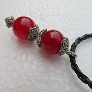 May include: A red gemstone necklace with two large, round beads and silver accents. The necklace is made of black braided cord.