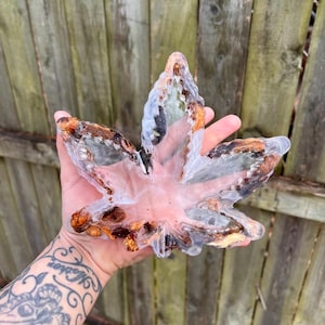 May include: A clear resin leaf-shaped tray with brown and white accents. The tray has a glossy finish and is held in a hand. The background is a wooden fence.