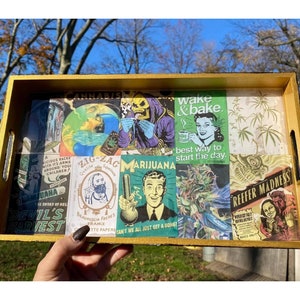 Puede incluir: Una bandeja rectangular de madera con un marco pintado de oro. El interior de la bandeja presenta un collage de im&aacute;genes y texto de estilo vintage relacionados con la cultura del cannabis, incluyendo las frases "Wake & Bake" y "Reefer Madness".