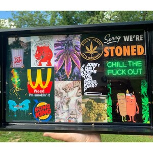 Puede incluir: Una bandeja rodante rectangular negra con un collage de im&aacute;genes y texto. El collage incluye im&aacute;genes de cannabis, dinero y personajes de dibujos animados. El texto incluye "Sorry We're Stoned" y "Chill the F*ck Out".