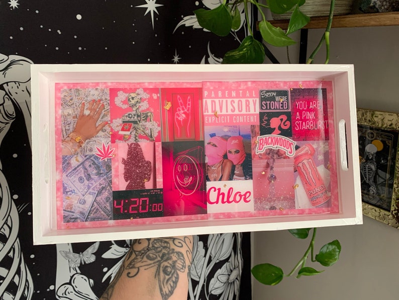Puede incluir: Una bandeja rectangular blanca con un interior rosa que presenta varias im&aacute;genes rosas y rojas, incluyendo dinero, un esqueleto y el texto "PARENTAL ADVISORY". La bandeja tiene asas blancas y una capa protectora transparente.