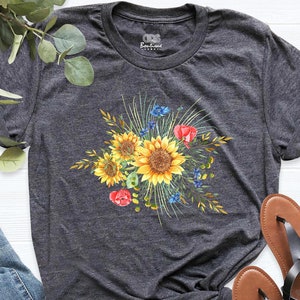 May include: A dark gray t-shirt with a floral design featuring sunflowers, red flowers, and blue wildflowers. The design is centered on the shirt.