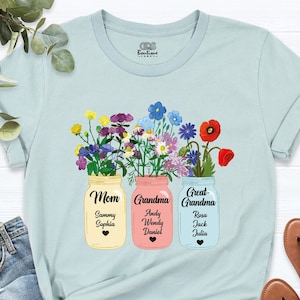 May include: Light blue t-shirt with a floral design featuring three mason jars with the words "Mom", "Grandma", and "Great-Grandma" and names of family members inside each jar.