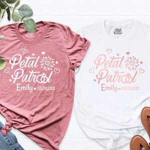 Puede incluir: Dos camisetas blancas con un dise&ntilde;o rosa que dice "Petal Patrol" con un girasol y corazones. El texto tambi&eacute;n incluye el nombre "Emily" y la fecha "03.08.2021".