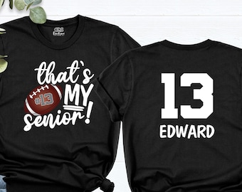 May include: Black t-shirt with white text that says "that's my senior!" and a football with the number 13 on it. The back of the shirt has the number 13 and the name "EDWARD" in white.