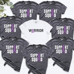 May include: Seven gray t-shirts with purple ribbons and the text "SUPPORT SQUAD" printed on them. One white t-shirt with a purple ribbon and the text "WARRIOR" printed on it.