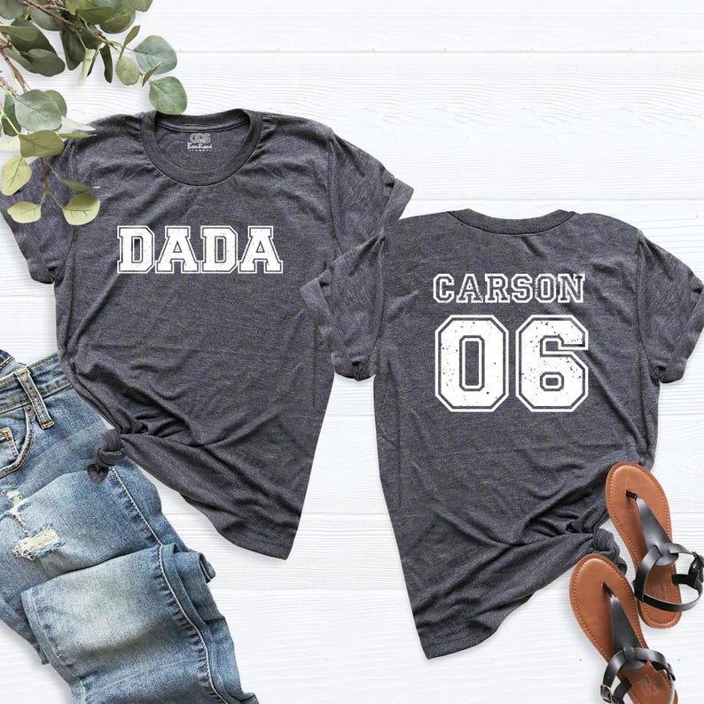 May include: Two gray t-shirts with white text. One shirt says "DADA" and the other says "CARSON 06".