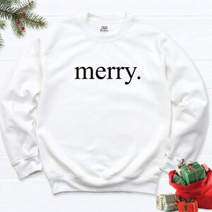 May include: White sweatshirt with the word "merry" printed in black on the front.