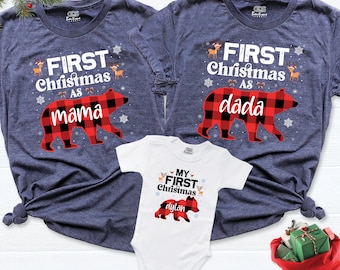 May include: Three Christmas-themed shirts. Two navy blue t-shirts with "FIRST Christmas as mama" and "FIRST Christmas as dada" printed on them, featuring a red and black plaid bear graphic. A white onesie with "MY FIRST Christmas" and a plaid bear graphic.