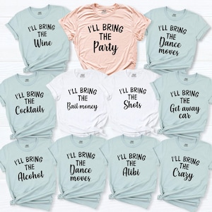 May include: A collection of eleven short-sleeved t-shirts in light blue, white, and peach. Each shirt features black text stating phrases such as I'll bring the wine, party, dance moves, cocktails, bail money, shots, get away car, alcohol, or alibi.