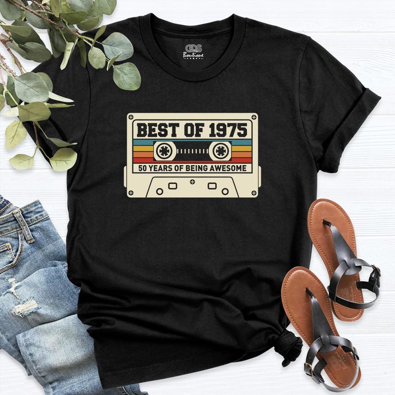 K&ouml;nnte beinhalten: Schwarzes T-Shirt mit einem Vintage-Kassettenband-Motiv, auf dem "Best of 1975 50 Years of Being Awesome" steht.