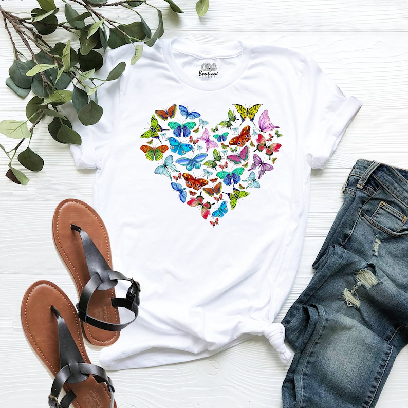 May include: White t-shirt featuring a heart-shaped design made up of colourful butterflies.