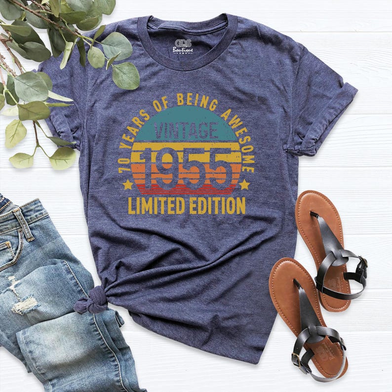 Op de afbeelding: Een marineblauw T-shirt met een vintage ontwerp uit 1955. Het shirt heeft een zonsondergangafbeelding met de tekst "70 Years of Being Awesome Vintage 1955 Limited Edition".