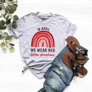 May include: A gray t-shirt with a red rainbow and the text "In April We Wear Red Autism Acceptance".