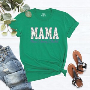 Puede incluir: Camiseta verde con la palabra "MAMA" en letras blancas con un patr&oacute;n floral. Los nombres "Noah", "Sunny" y "Rachel" est&aacute;n escritos en morado debajo de la palabra "MAMA".