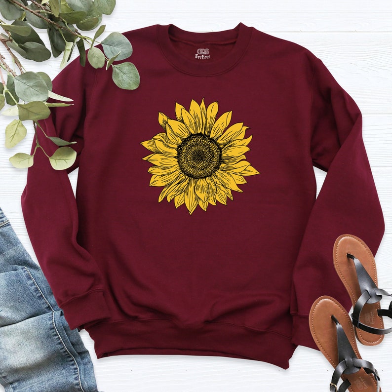 May include: A maroon sweatshirt with a yellow sunflower graphic print.
